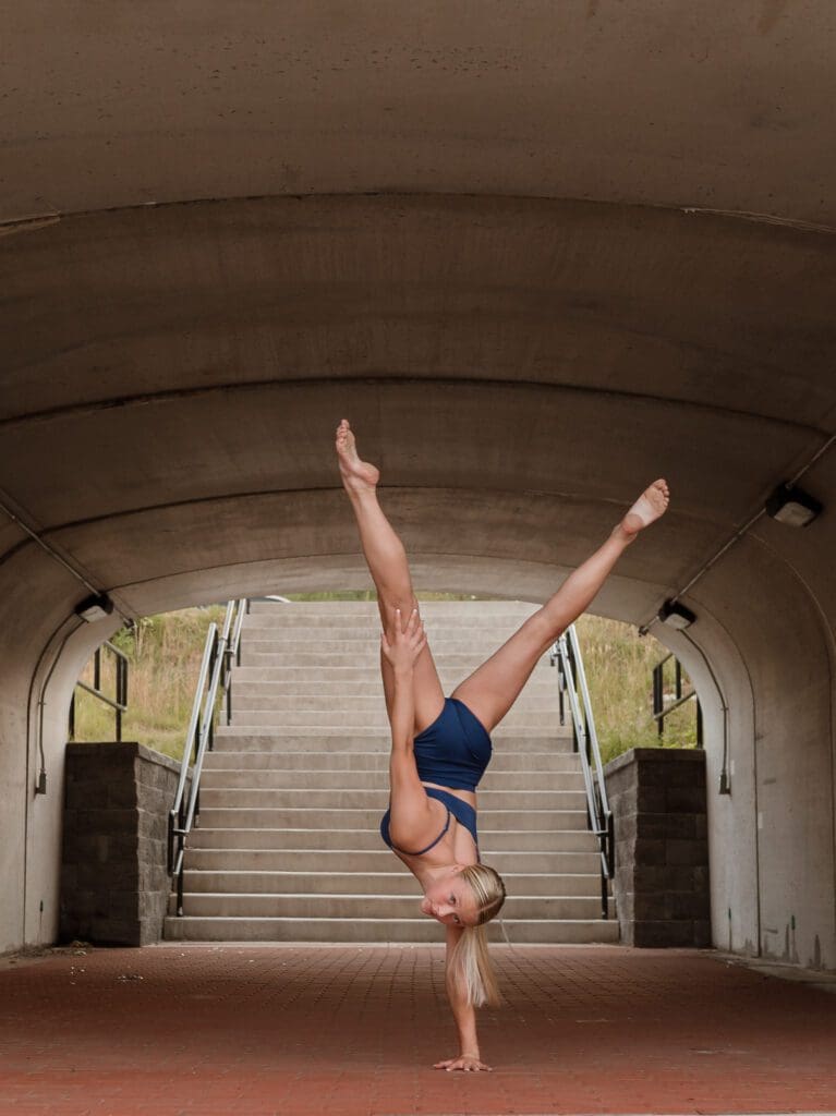 Woman in blue doing handstand under bridge.