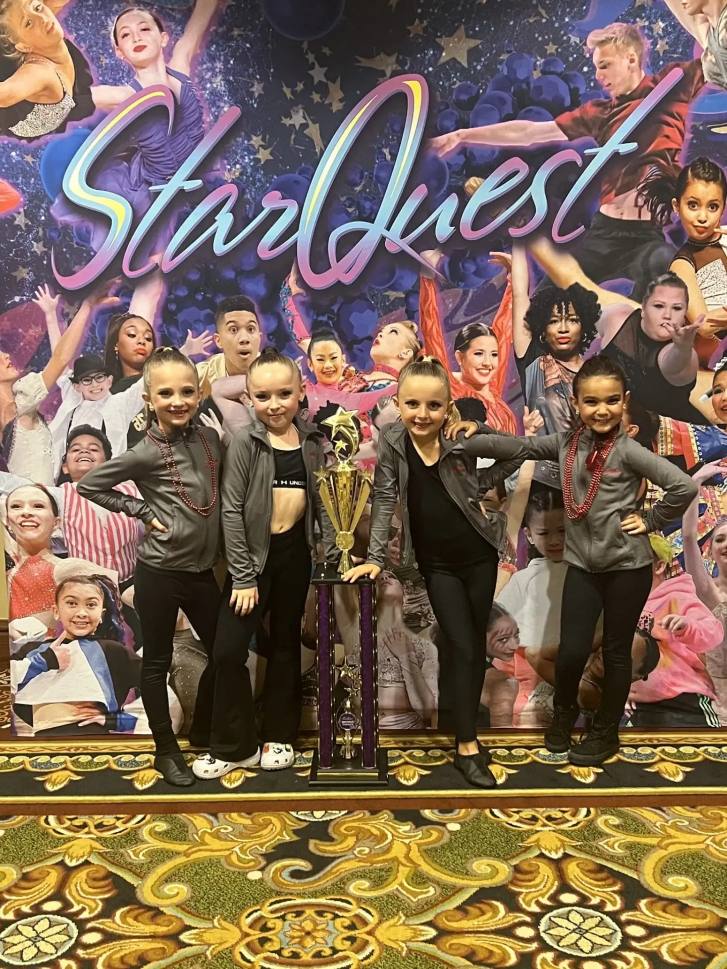 Two girls in grey jackets with a trophy.