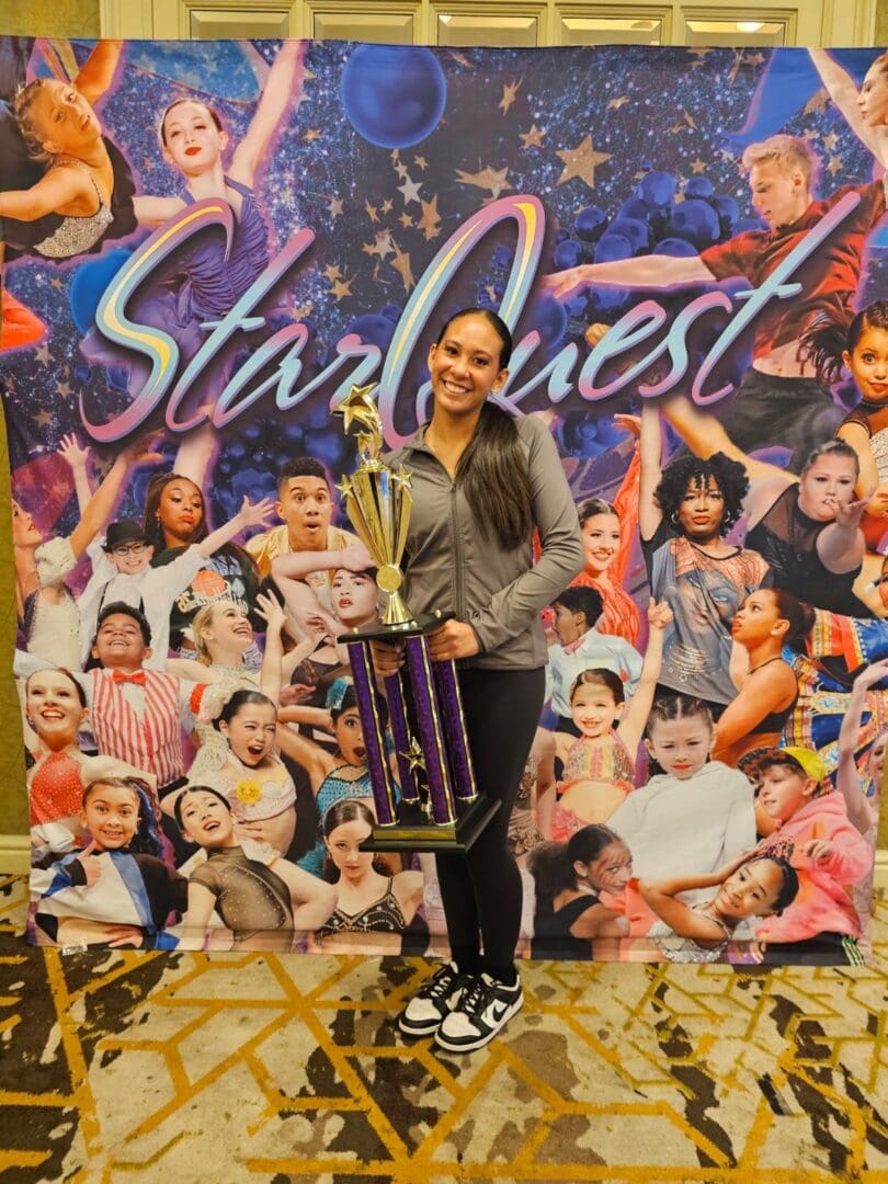 Young woman proudly holding a trophy in front of a colorful 'Starquest' backdrop.