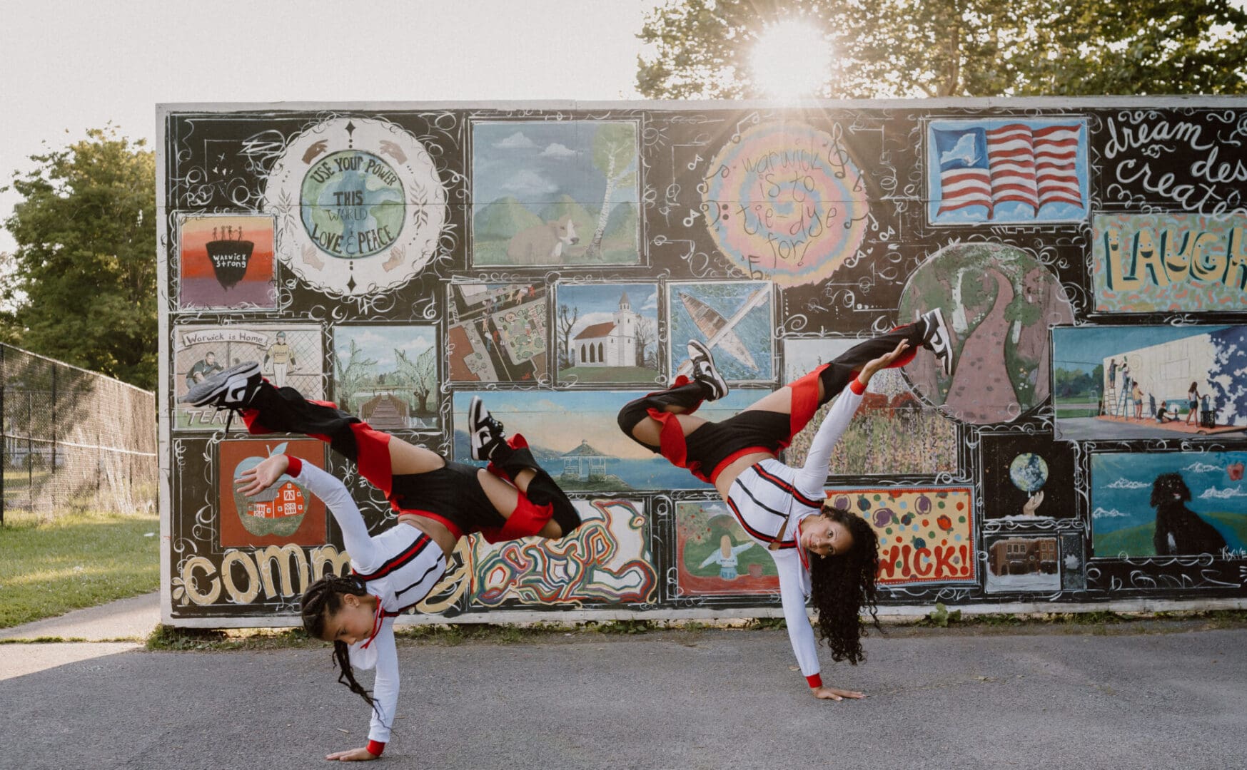 Two performers in red and black doing synchronized breakdance moves outdoors.