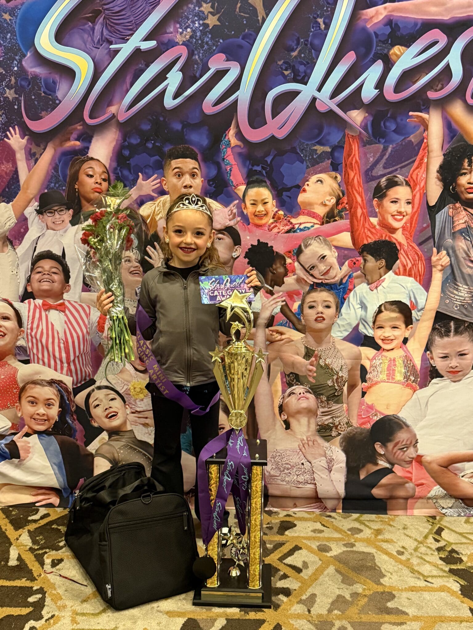 Young girl in a dance costume holding a trophy and flowers on stage.