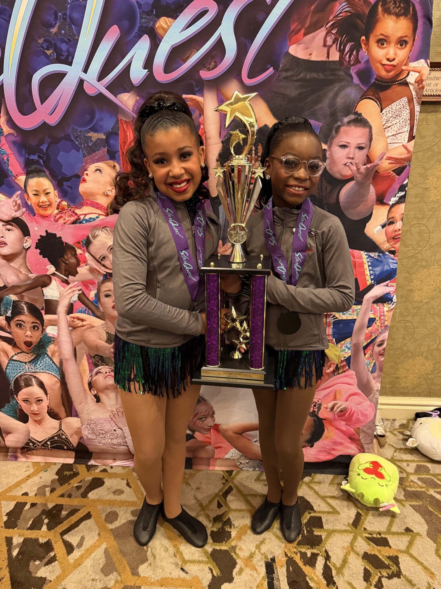 Two young girls proudly holding a large trophy at an event.