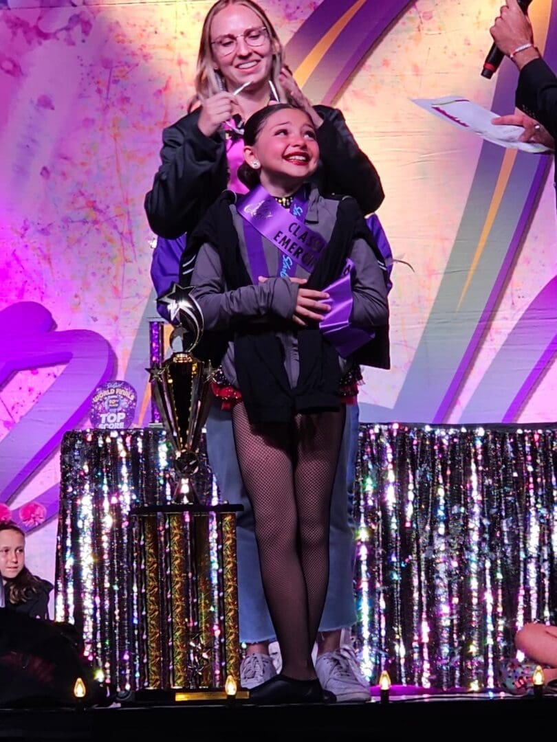 A joyful woman in a wheelchair on stage holding a trophy.