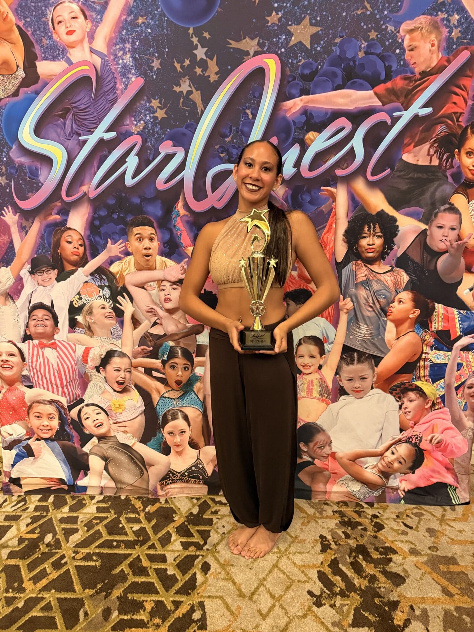 Smiling dancer holding trophy at colorful StarQuest backdrop